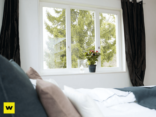 Modernes Schlafzimmer mit großen Fenstern, Blick ins Grüne und einer Zimmerpflanze.
