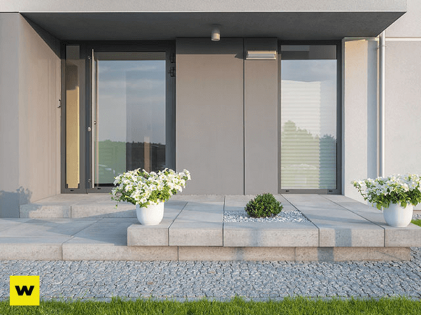 Moderner Hauseingang mit großen Fenstern, Steinfliesen und weißen Blumentöpfen im Vorgarten.